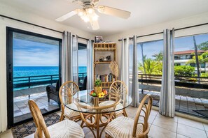 A glass-top dining table with wicker chairs, a ceiling fan, and a view of the ocean through large sliding doors. - Casa De Emdeko 219 (Kailua-Kona)