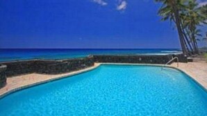 Une piscine d’eau cristalline, d’un bleu éclatant, avec vue sur l’océan et les palmiers.
