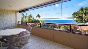 A balcony with a view of the ocean, a table, and chairs.