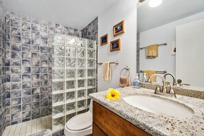 A bathroom with a glass shower enclosure, a sink with a granite countertop, and a mirror above the sink.