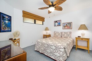 A bedroom with a bed, two bedside tables, a ceiling fan, a window with blinds, and wall-mounted artwork.