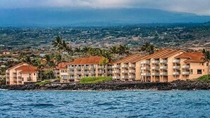 Un hôtel situé en bord de mer, doté de nombreux balcons, d’une côte rocheuse et de palmiers en arrière-plan.