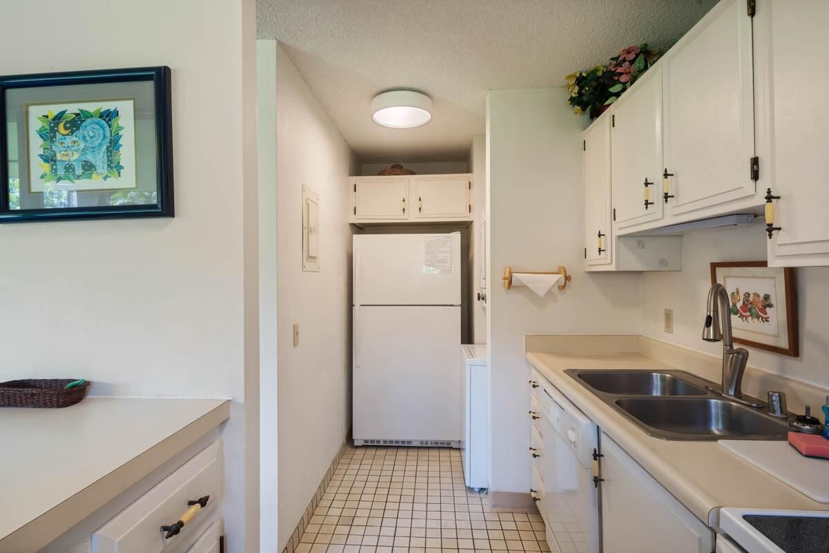 A compact kitchen with white cabinets, a refrigerator, and a sink.