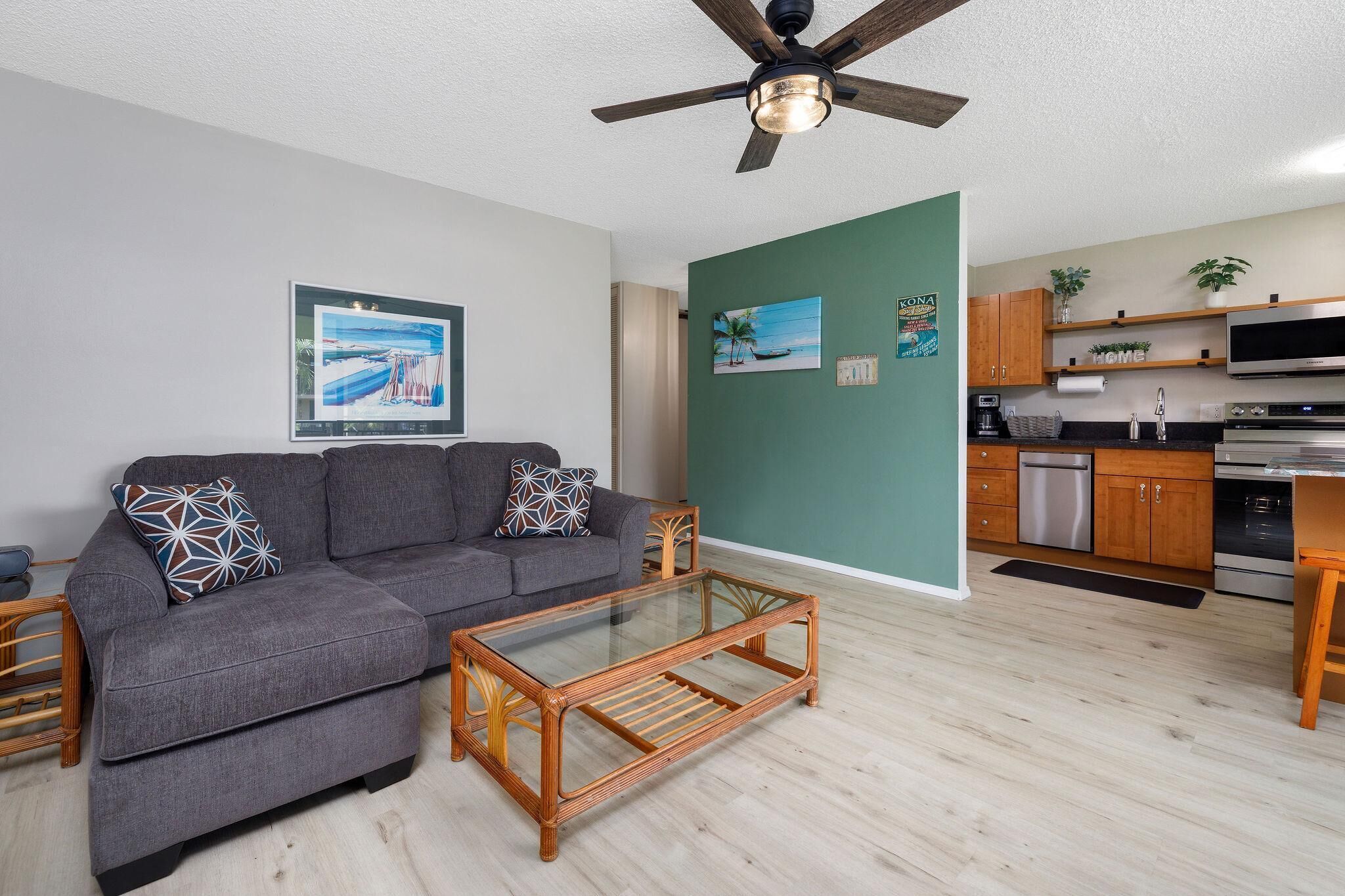 A modern living room with a grey sofa, a glass coffee table, and a ceiling fan.