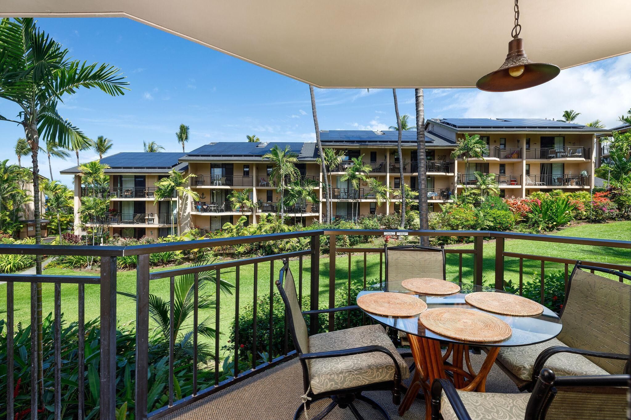 A balcony with outdoor seating, a hanging light fixture, and a view of a hotel building with multiple balconies and palm trees.