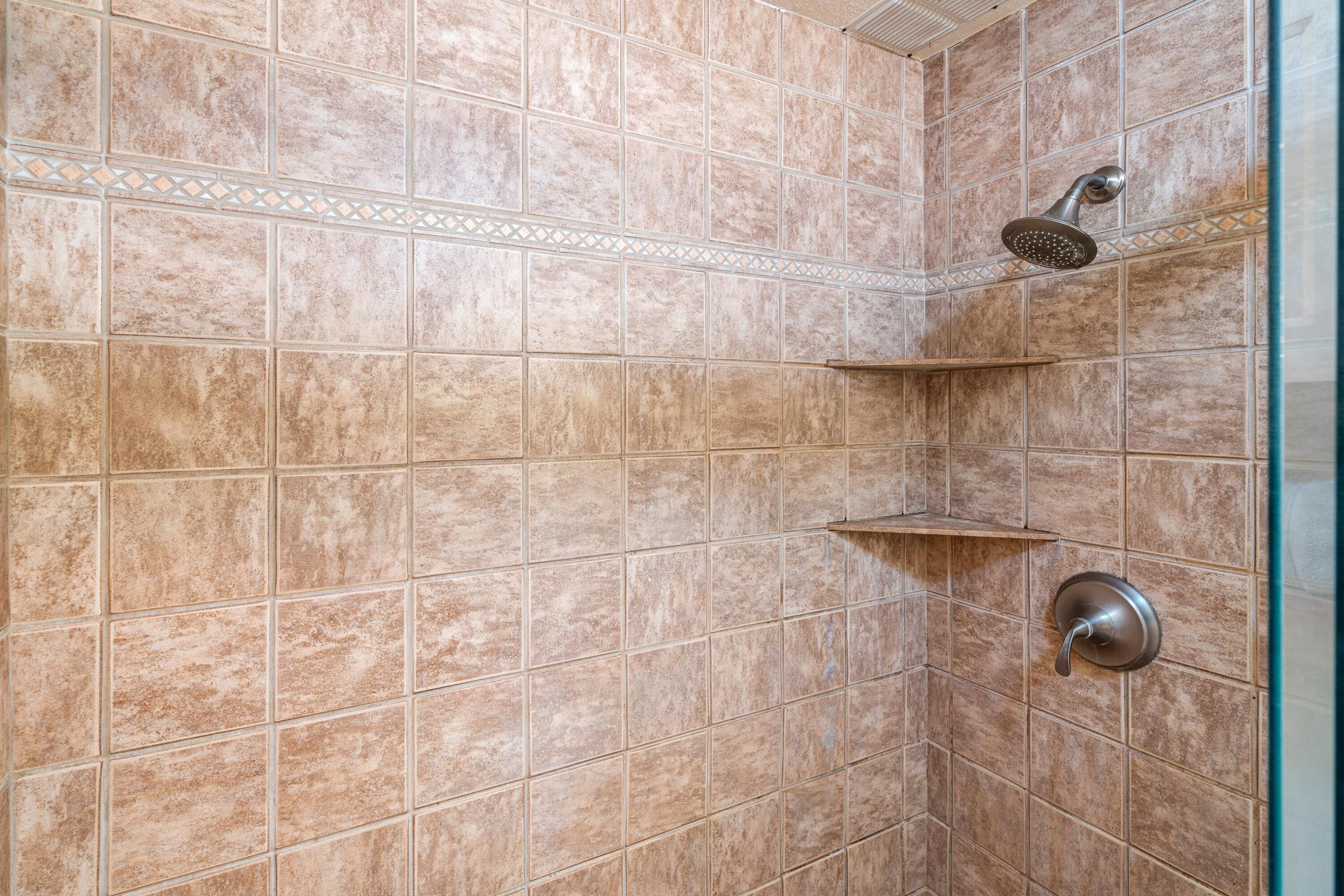 Un espacio de ducha con azulejos color beige, un cabezal de ducha y un panel de control de pared.