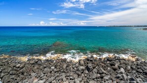 A rocky shoreline with clear turquoise water and a distant coastline. - Sea Village 4-205 (Kailua-Kona)