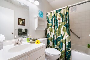 A bathroom with a white sink, a toilet, and a shower with a tropical leaf-patterned curtain.