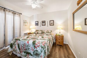 A bedroom with a bed, two bedside tables with lamps, a ceiling fan, and a large mirror.