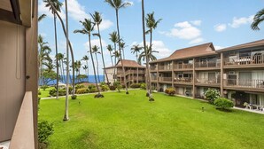 A hotel with multiple floors, a well-maintained lawn, and tall palm trees. - Kona Isle C24 (Kailua-Kona)