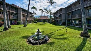A hotel courtyard with a fountain, palm trees, and a well-maintained lawn. - Kona Isle C24 (Kailua-Kona)