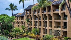 Un hôtel à plusieurs étages, chacun doté de balcons, entouré d’une végétation luxuriante et de palmiers.