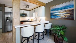 Une cuisine moderne avec des meubles blancs, un îlot central doté de tabourets et un grand tableau accroché au mur.