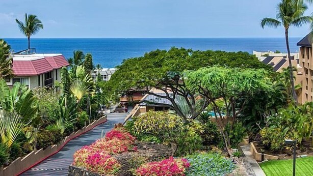 Un complexe hôtelier tropical offrant une vue sur l’océan, une végétation luxuriante et un sentier menant à un bâtiment doté d’un toit rouge.