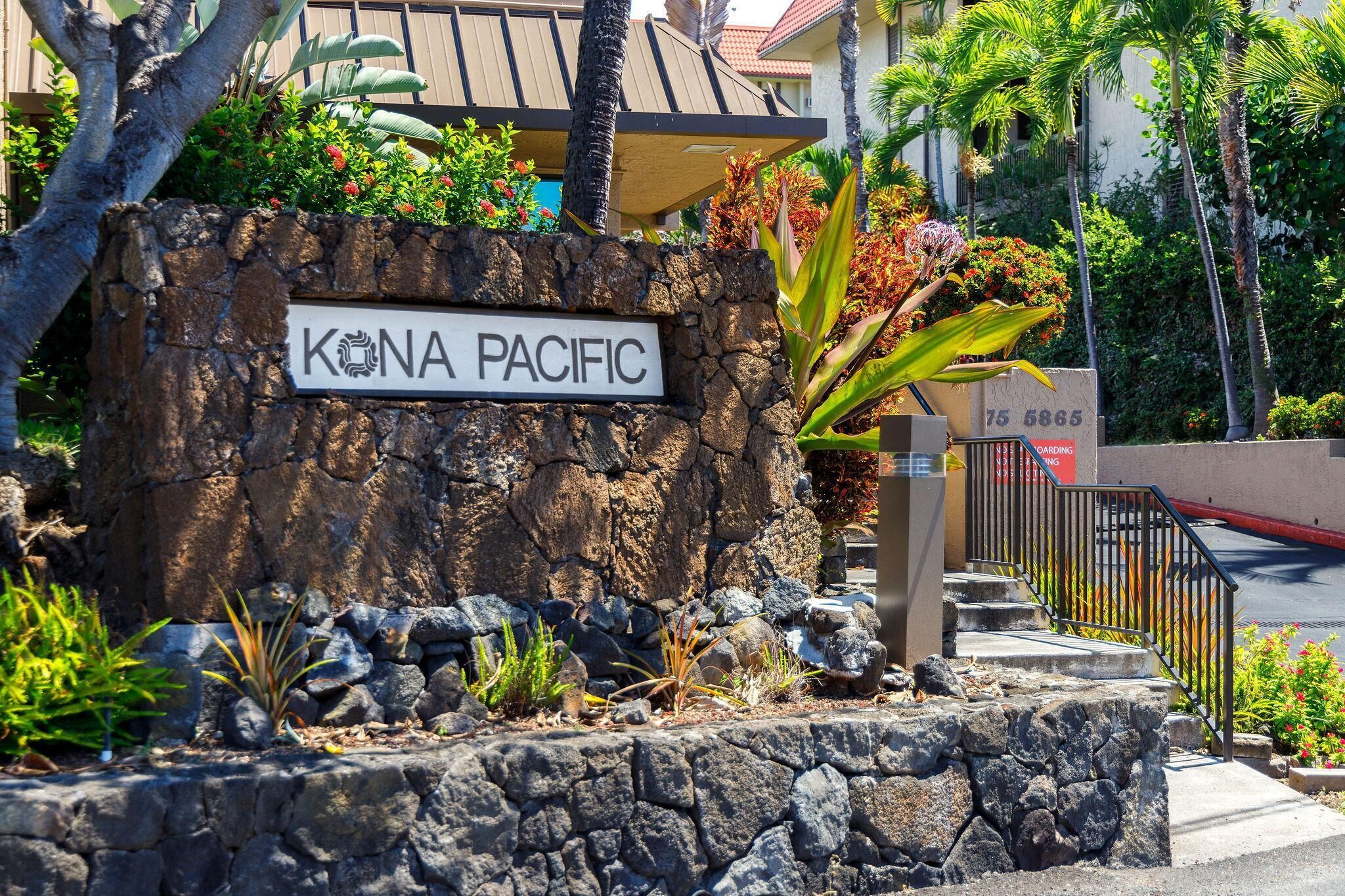 A sign with "KONA PACIFIC" written on it, surrounded by rocks and plants.