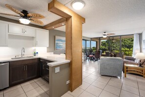 Een moderne keuken met een centraal eiland, een eethoek met terrasstoelen, en een groot raam met uitzicht op groen.