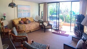 A spacious room with a large bed, multiple seating areas, a television, and a balcony with a view of the outdoors. - Kalani Kai 105 (Kailua-Kona)