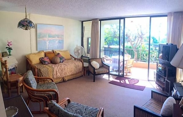 Una habitación amplia con una cama grande, varios rincones para sentarse, televisión y un balcón con vistas al exterior.