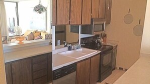 A kitchen with wooden cabinets, a microwave, a sink, and a dishwasher. - Kalani Kai 105 (Kailua-Kona)