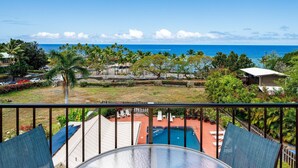 A balcony with a glass table and chairs overlooking a swimming pool and a view of the ocean. - Kahaluu Bay Villas 304 (Kailua-Kona)