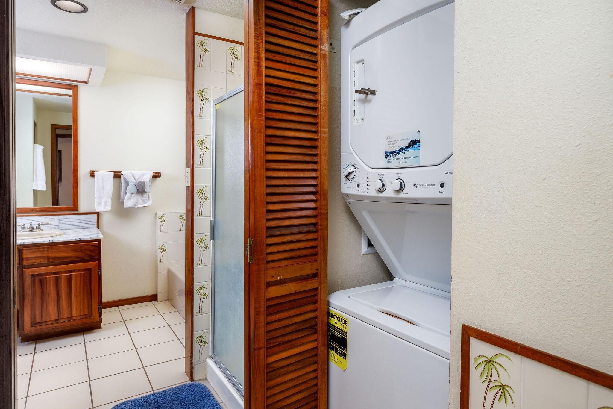 Ein Badezimmer mit einem Holzbadezimmerhocker, einer weißen Waschmaschine und einer Duschkabine aus Glas.