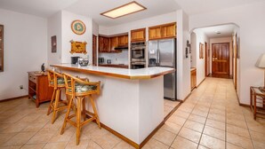 A kitchen with a central island, wooden cabinets, and a refrigerator. - Kahaluu Bay Villas 304 (Kailua-Kona)