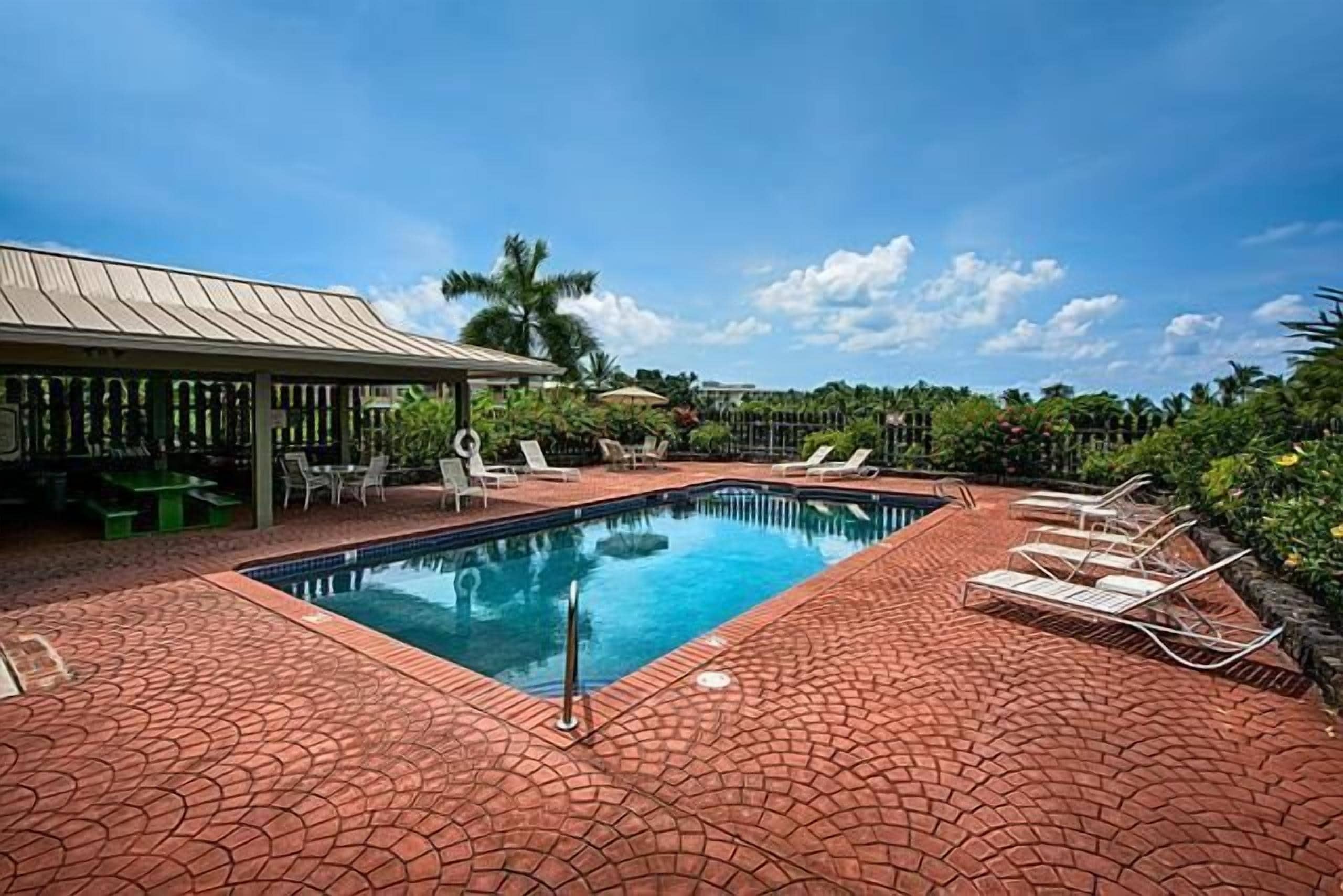 A rectangular swimming pool with a tiled deck, surrounded by lounge chairs and a covered seating area.