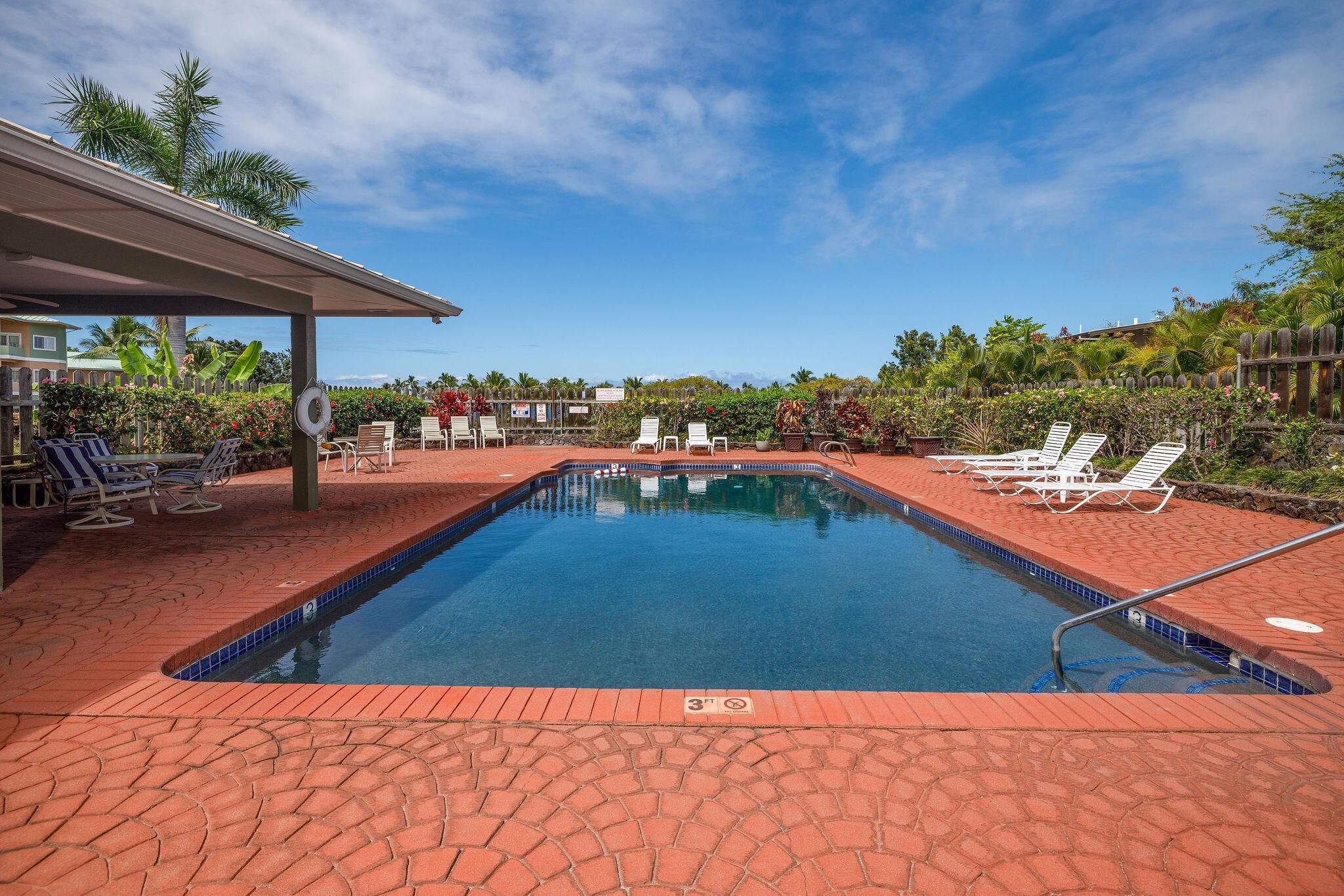 A rectangular pool with a 3-foot depth marker, surrounded by red brick flooring and white lounge chairs.