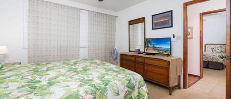 Un dormitorio con cama, cómoda, televisor y ventilador de techo.