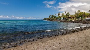 A beach with clear blue water, a rocky shoreline, and a line of palm trees. - Kahaluu Bay Villas 304 (Kailua-Kona)