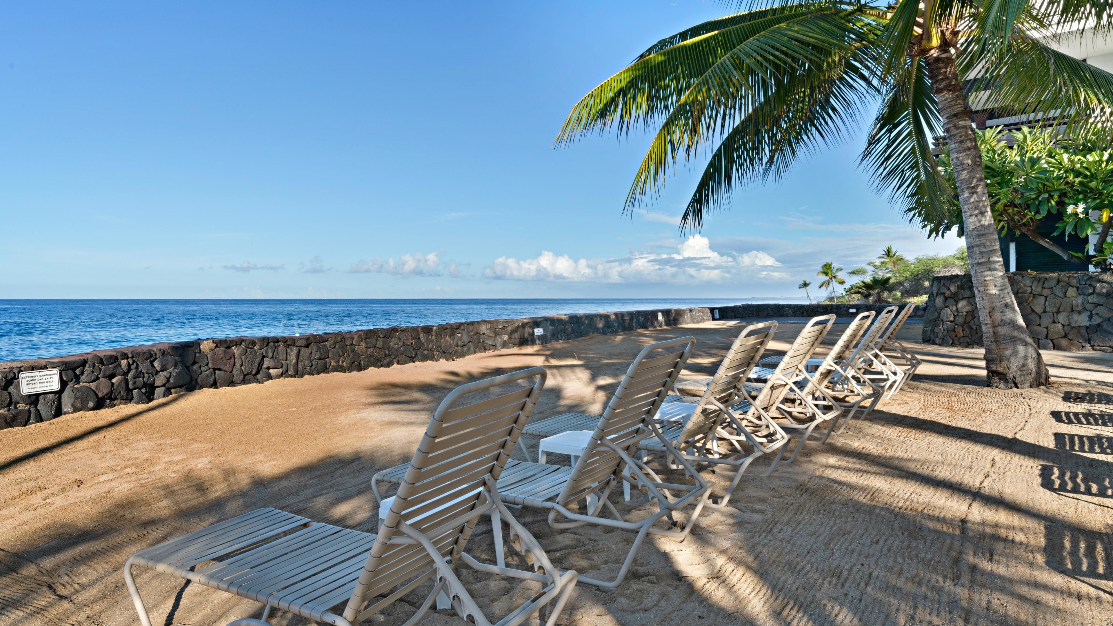 A beach with lounge chairs and a stone wall.