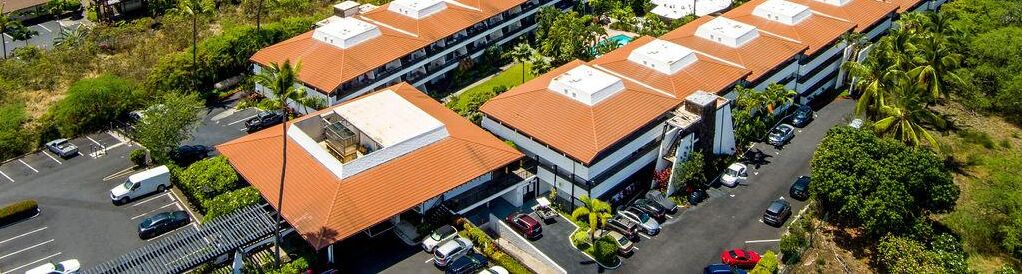 Ein mehrstöckiges Hotel mit rotem Ziegeldach, Parkplatz und umliegender Bepflanzung.
