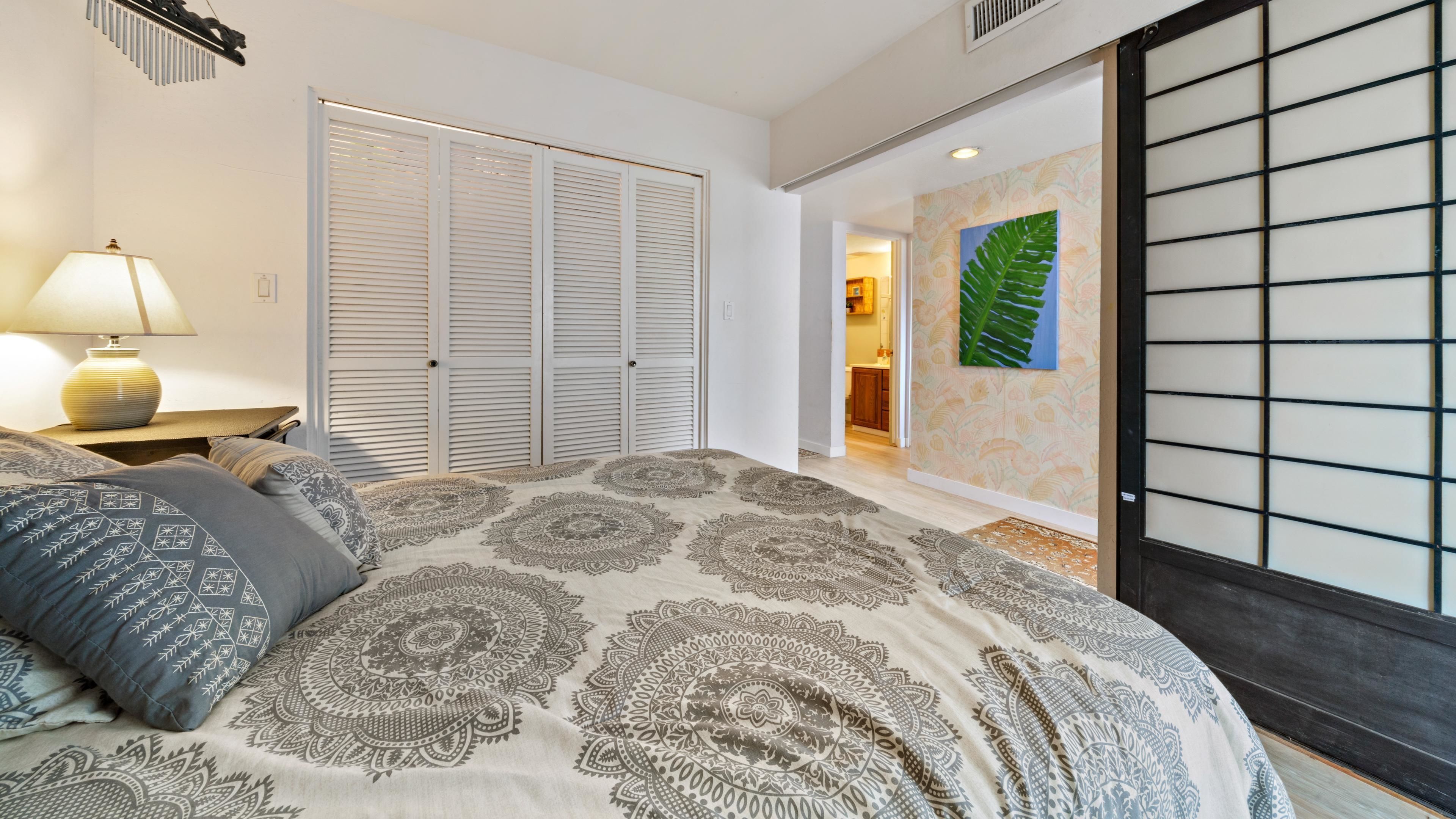 A bedroom with a large bed, a bedside table with a lamp, a wardrobe, and a door leading to a bathroom.