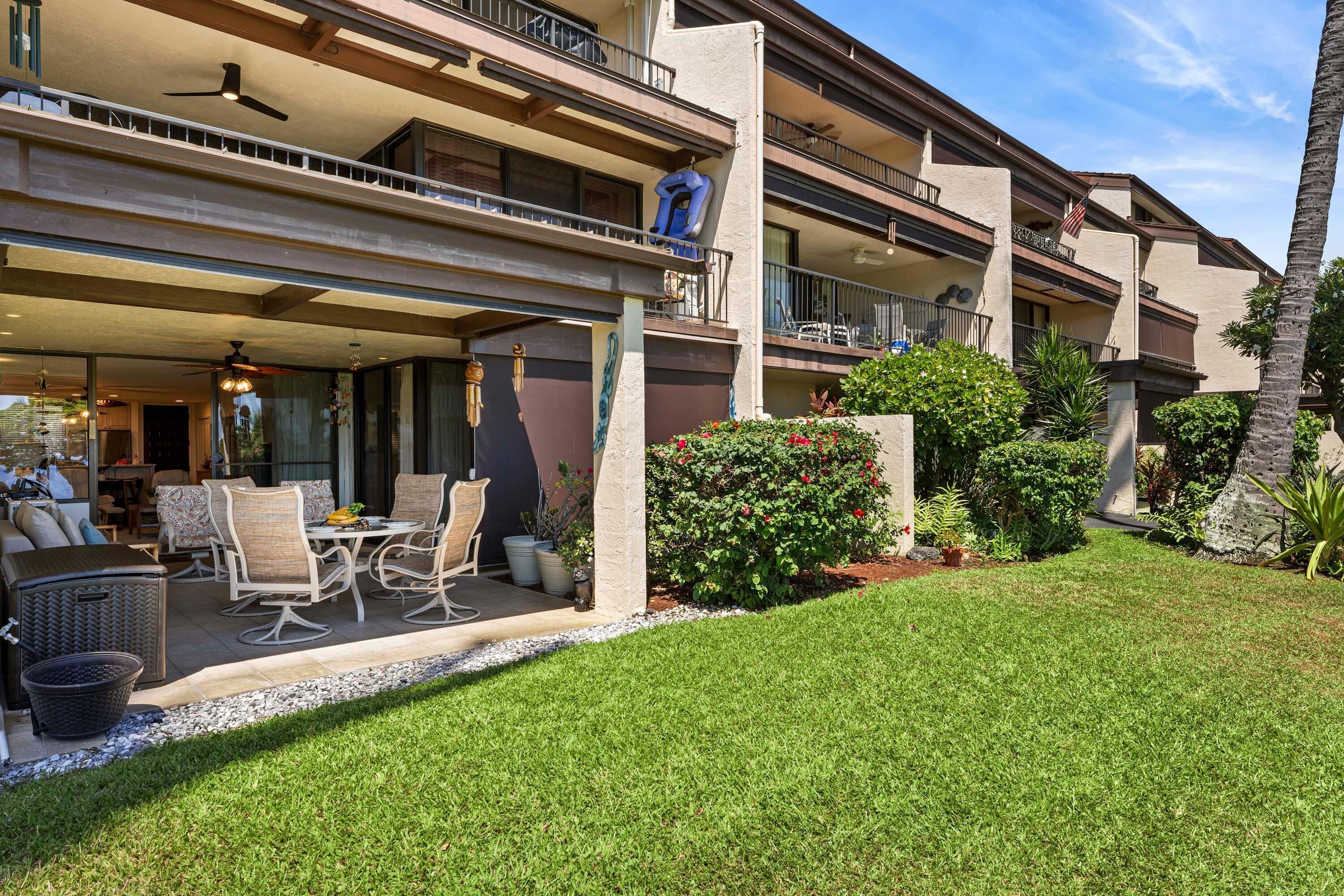 A multi-story residential building with a covered patio area, outdoor furniture, and a well-maintained garden.