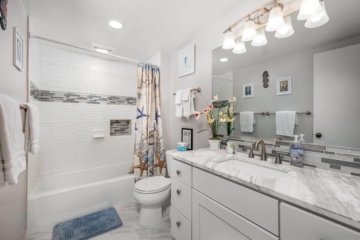 A modern bathroom with a bathtub, toilet, and a vanity with a large mirror and multiple faucets.