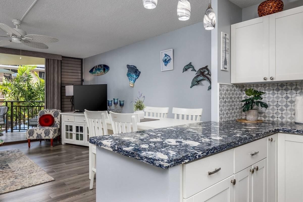 Una cocina moderna con armarios blancos, encimera de granito y detalles decorativos en la pared.