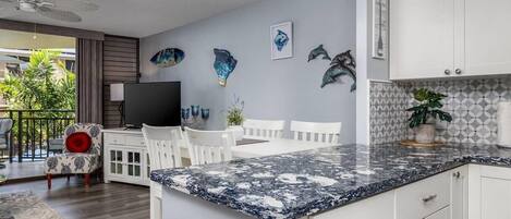 Una cocina moderna con armarios blancos, encimera de granito y detalles decorativos en la pared.