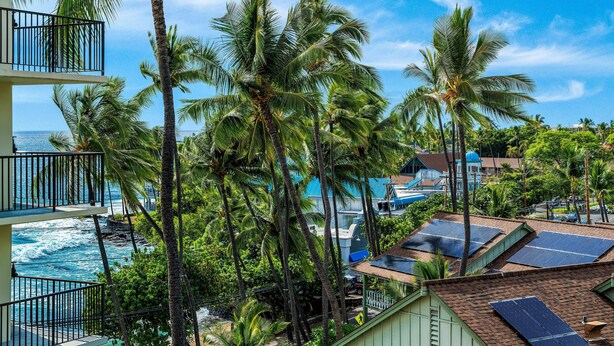 A coastal hotel with multiple floors, palm trees, and solar panels on the roof. - Kona Alii 608 (Kailua-Kona)