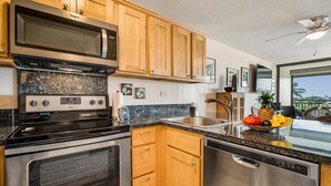 A kitchen with wooden cabinets, stainless steel appliances, granite countertops, and a fruit bowl. - Kona Alii 608 (Kailua-Kona)