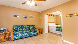 A room with a sofa, a bed, a ceiling fan, and a small table. - Kona Shores#130 (Kailua-Kona)