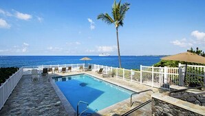 A pool with a white fence, a palm tree, and a view of the ocean. - Kona Shores#130 (Kailua-Kona)