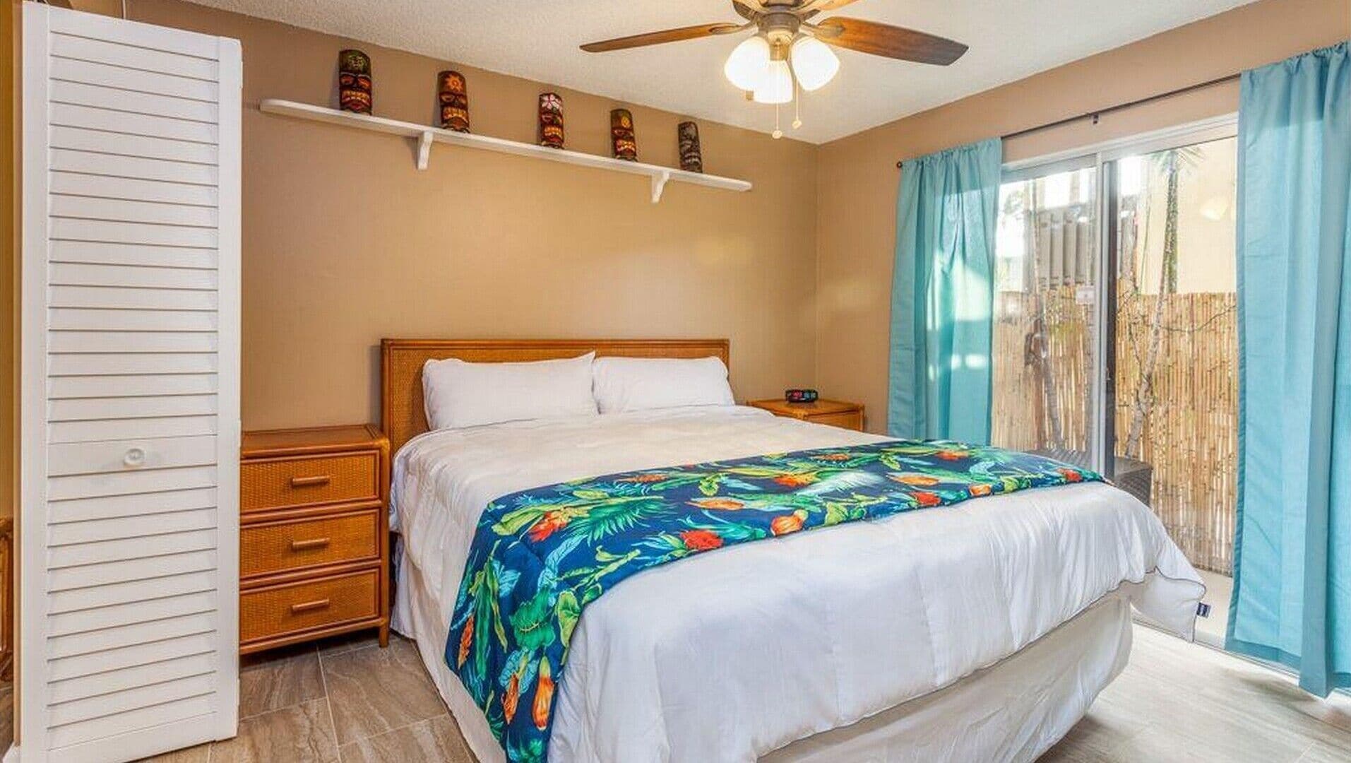 A bedroom with a bed, a nightstand, a drawer, a ceiling fan, and a window with curtains.