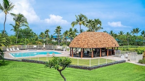 A pool area with a thatched-roof gazebo, surrounded by palm trees and a well-maintained lawn. - Keauhou Punahele#e-102 (Kailua-Kona)