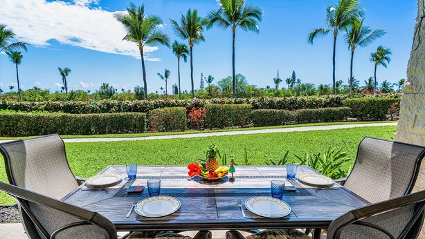 An outdoor dining area with a table set for two, surrounded by chairs with floral upholstery. - Keauhou Punahele#e-102 (Kailua-Kona)