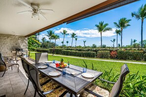 Un espace de restauration en plein air avec une table dressée pour quatre personnes, entourée de chaises, et une vue sur un jardin bien entretenu agrémenté de palmiers.