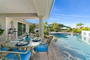 A poolside area with a table set for dining, surrounded by chairs, and a clear view of a swimming pool. - Kona Bubbles (Kailua-Kona)