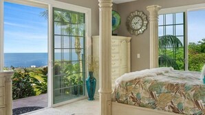 Ein Schlafzimmer mit großem Fenster, einem Bett, einer Kommode und einer Wanduhr.