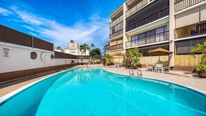A swimming pool with a no driving sign, outdoor seating, and a multi-story building in the background.