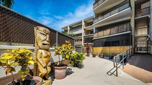 A courtyard with potted plants, a wooden statue, and a building with balconies.