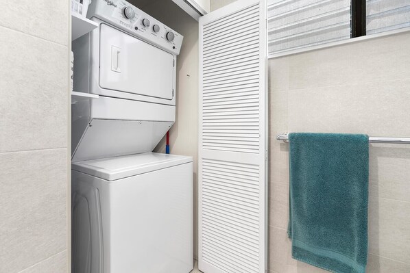 Un espace buanderie compact comprenant un lave-linge et un sèche-linge, un porte-serviettes et un placard avec une porte coulissante.